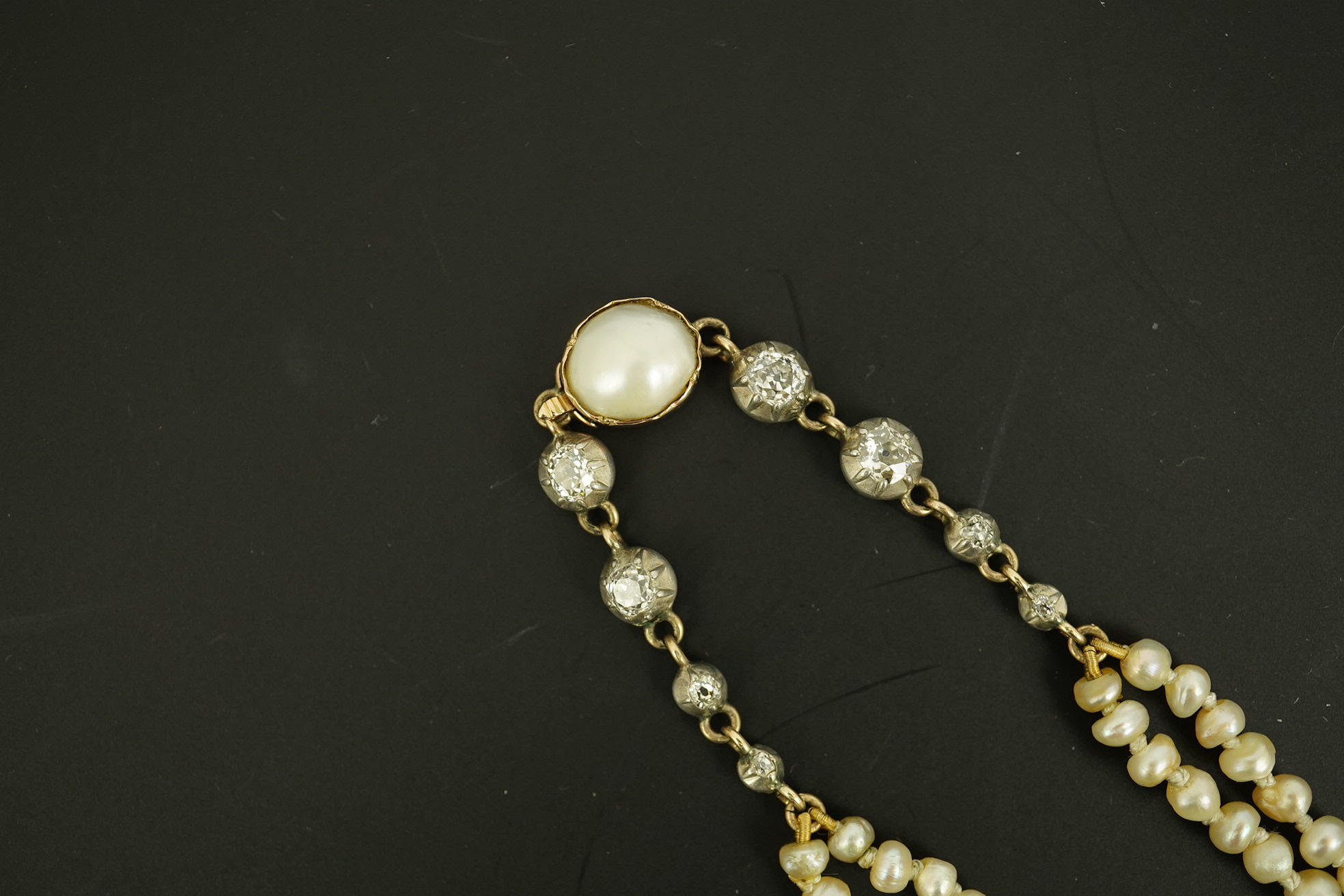 An antique twin strand baroque pearl necklace, with pearl set gold clasp bordered with single chain set with four graduated old mine cut diamonds